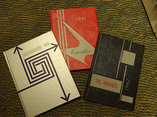 Three yearbooks lay on the ground. Their covers feature geometric and line patterns.