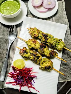 Serving pahadi kabab sticks on a plate with green chutney and onion slices