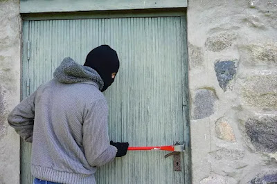 एक चोर घर के दरवाजे का ताला तोड़कर चोरी करने का प्रयास कर रहा है जिसने काले रंग के कपड़े से अपना मुंह ढका हुआ है