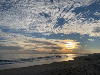 A picture of the sand, ocean, sky, and setting sun.