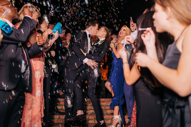 groom and groom kissing with friends blowing bubbles near them