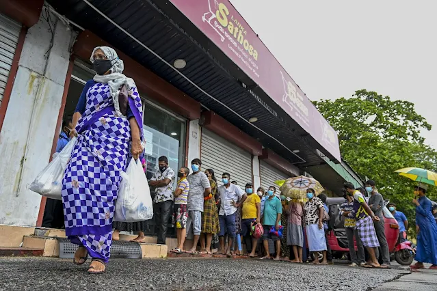 A woman carrying food bags walks past people queuing outside a state-run supermarket to buy essential food items in Colombo, Sri Lanka, on Sept. 3. ISHARA S. KODIKARA/AFP VIA GETTY IMAGES