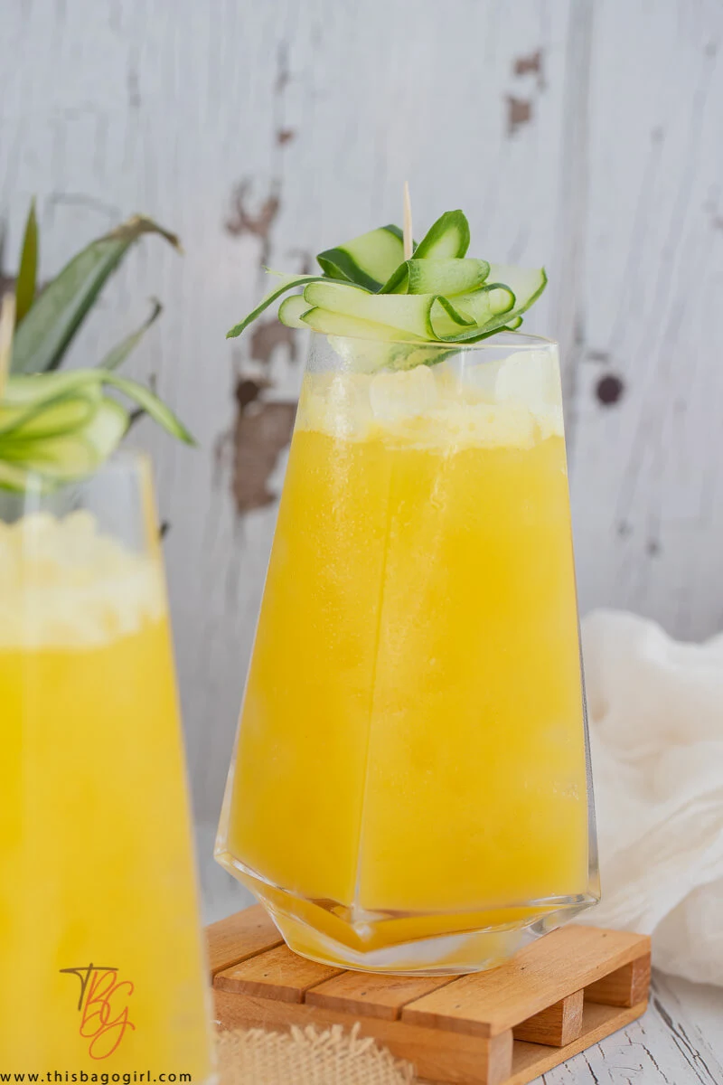 Close up picture of a glass of pineapple and cucumber juice with strips of cucumber on top for garnish.