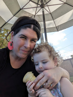 a mom and baby share an ice cream come under a large striped umbrella at Jason's Frozen Treats in Sioux City, Iowa