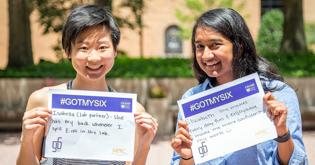 Two students standing in a courtyard with #GotMySix paper signs held up.