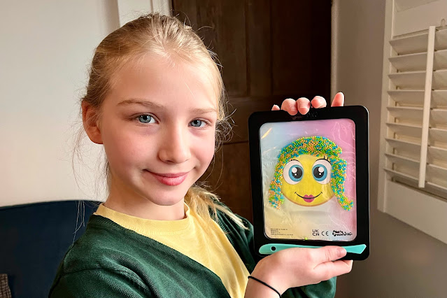 A tween girl holding up a doodlejamz jellypics board with an emoji she has given balls to