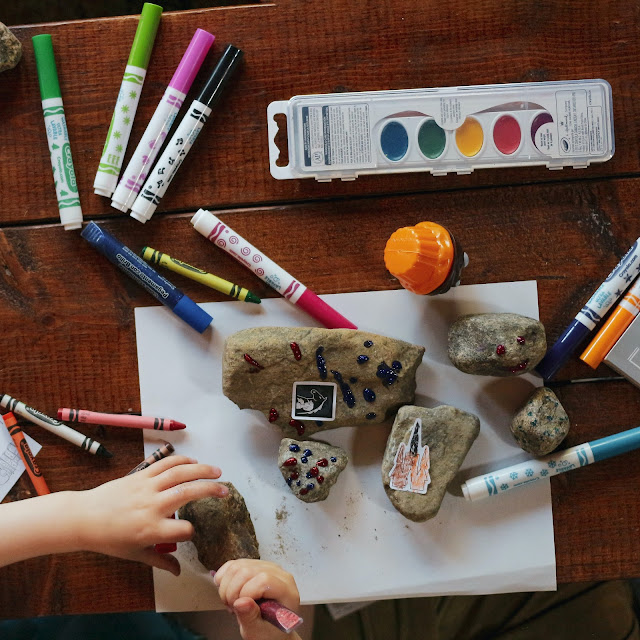 Child's hands using paint and crayons to decorate rocks