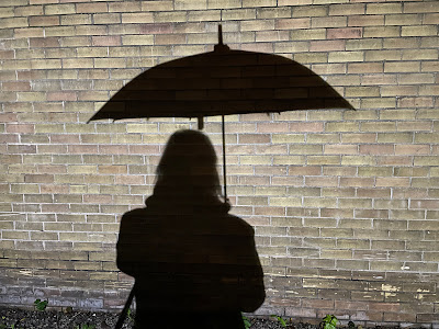 Shadow of person holding an umbrella with the handle of the umbrella near the body, covering the body under the umbrella.
