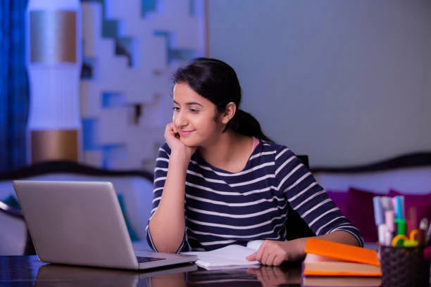 A girl is looking in laptop along reading books