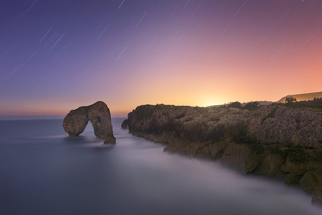 Fotografia de larga exposicion en el castro de las gaviotas con unas largas trazas de estrellas y una roca en medio del mar