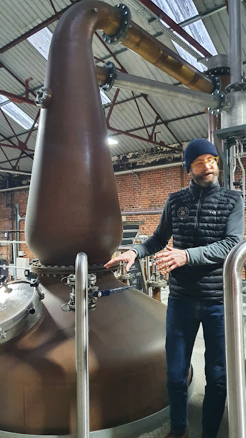 Man standin beside White Peak Distillery copper still for whisky making