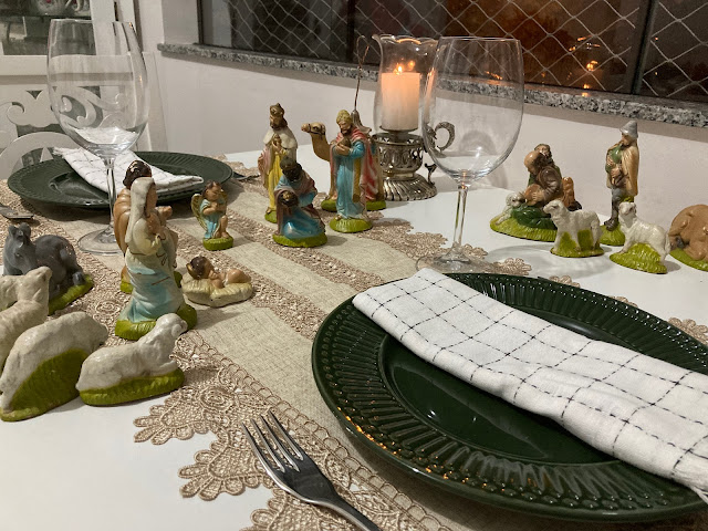 Mesa posta temática de presépio, trilho bege, prato verde, guardanapo branco com detalhes pretos e franjas, taças transparentes, talheres de peixe