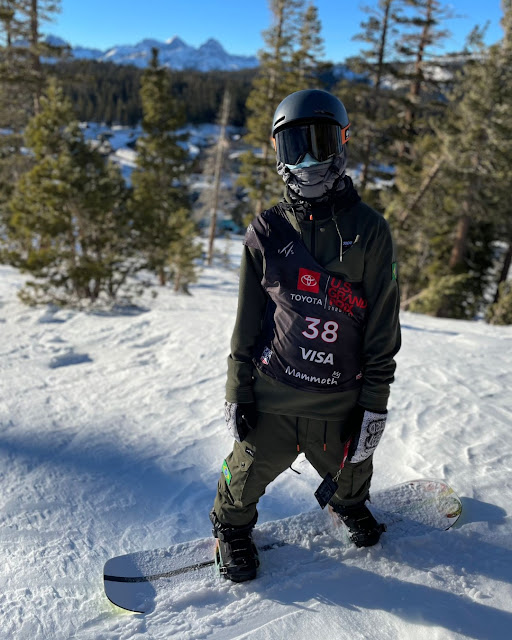 Augustinho Teixeira posa para foto encima do snowboard. Ele está todo coberto com agasalho e capacete com viseira