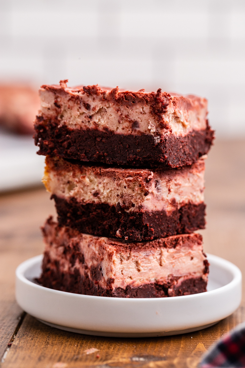 Photo of 3 Keto Red Velvet Cheesecake Brownies stacked on a small white serving plate.
