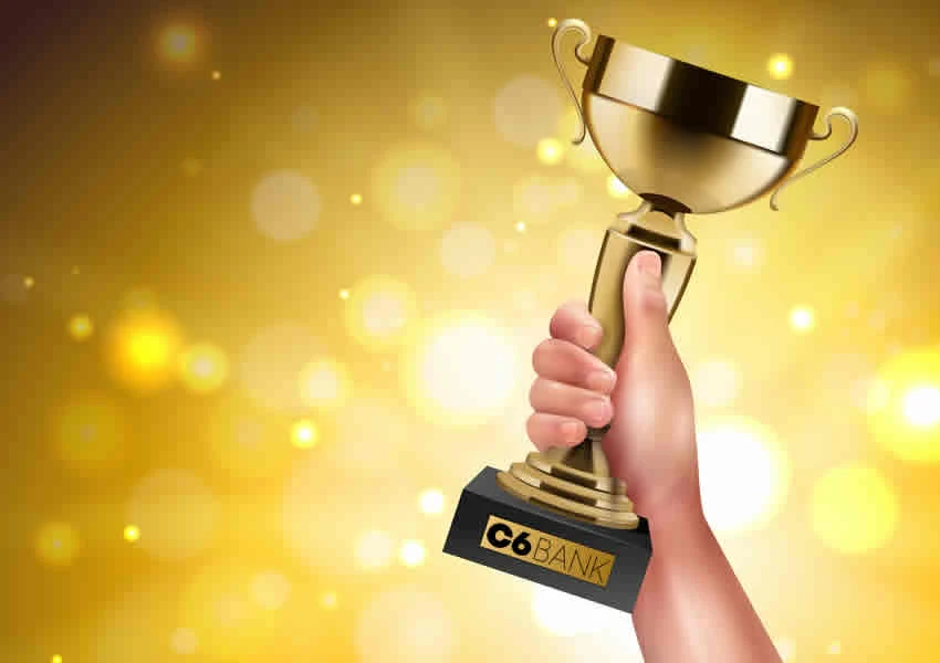 Imagem mostra uma mão erguida segurando um troféu que tem o nome do Banco C6 Bank gravado na base.