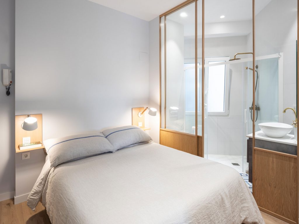 Dormitorio con mesitas voladas y puerta corredera de cristal y madera de acceso al baño