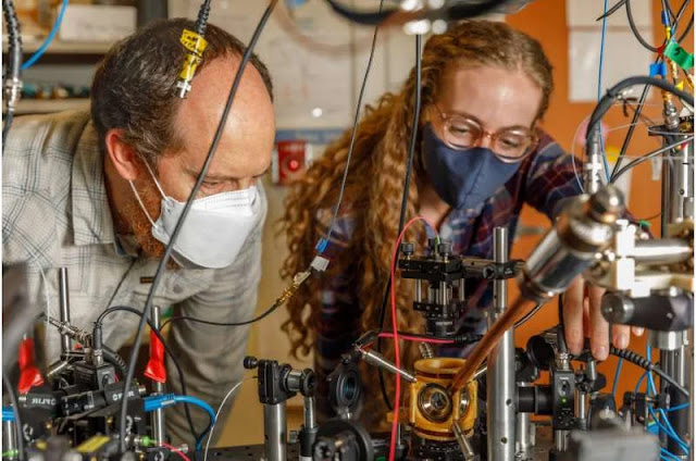El científico de Sandia National Laboratories Peter Schwindt, a la izquierda, y la científica postdoctoral Bethany Little examinan el paquete de vacío sostenido en una montura amarilla impresa en 3D. Crédito: Bret Latter