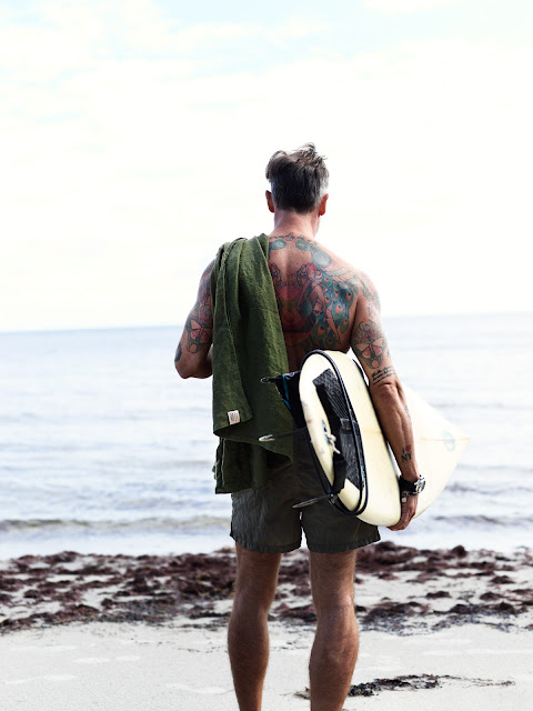 en man tittar på havet, håller en linnebadlakan på axeln och surfbreda