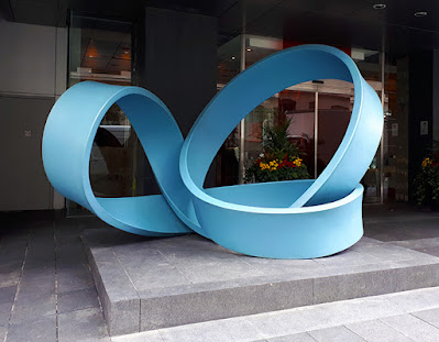 Large sculpture on the street, of a blue sinewy object, resembling a very large rubber band