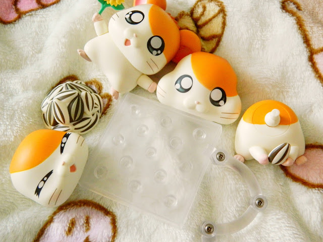 A photo showing a collection of figure parts to assemble. The figure is of an orange and white hamster character called Hamtaro. The parts include several facts, bodies and accessories, such as a sunflower and seeds.