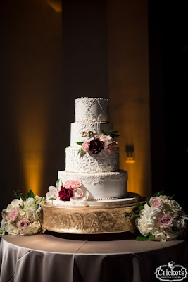 four tier white wedding cake on gold stand with flowers