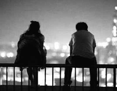 A man and woman sitting on a railing looking out over a city