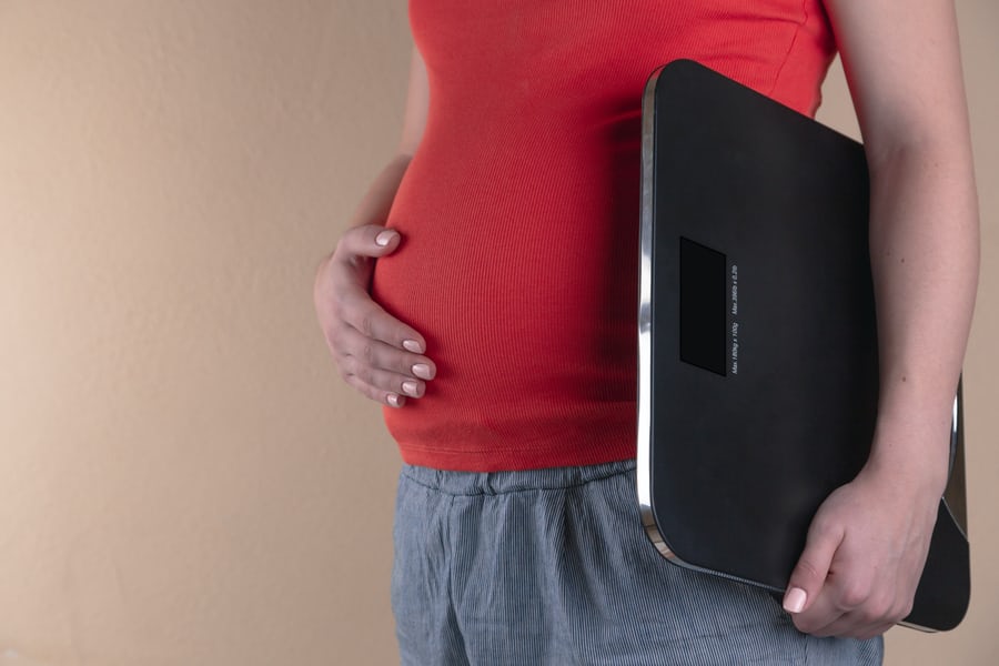 A pot-bellied man in red shirt and gray pants holding a weight loss scale and stroking his belly.