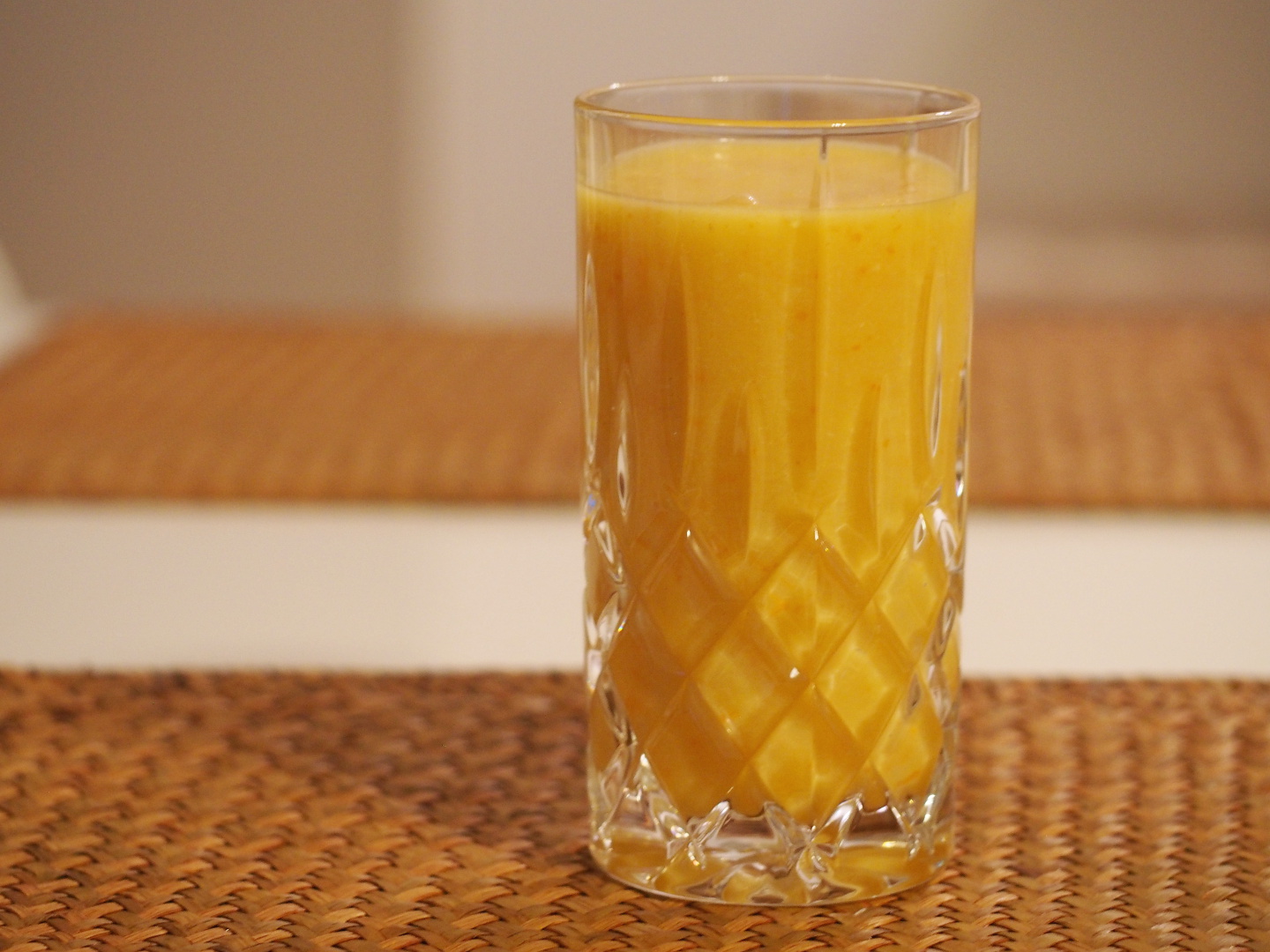 Ein gut gefülltes Glas mit dem Orangen-Kaki Smoothie. Der Smothie hat eine gelb-orangene Farbe.