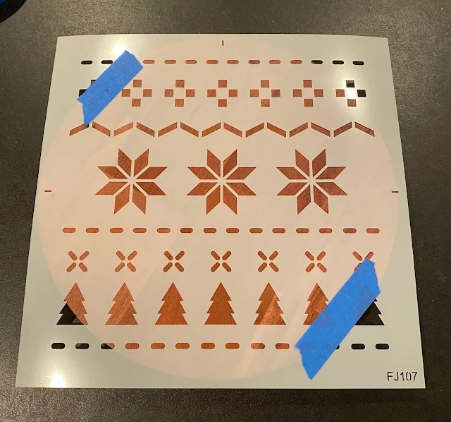 Photo of a Christmas sweater stencil taped on a round wooden tray.