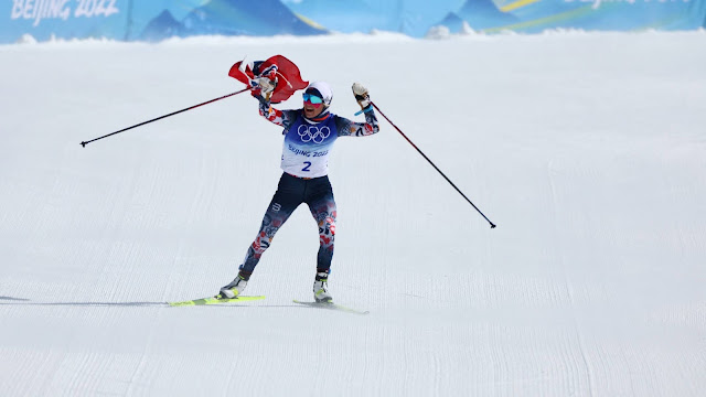 Therese Johaug nos metros finais da prova já comemorando. Ela esquia enquando carrega a bandeira da noruega com o braço direito