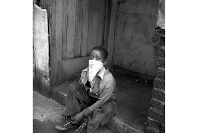 black and white photograph of African-American young boy with kerchief mask seated on stoopn in New Rork City while playing "cops and robbers", circa 1946-1950