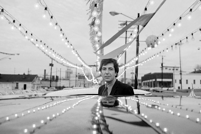 black and white photograph of Leonard Cohen in a car sales lot with strings of light in Nashville