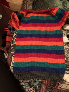 The sweater laid flat and turned right side up. There are exactly 4 repeats of the 4 color sequence followed by gray ribbing at the bottom edge. There are furry cat feet touching the right hand side of the sweater.