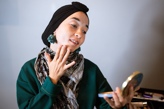 A lady in a head scarf admiring herself on her mirror compact.