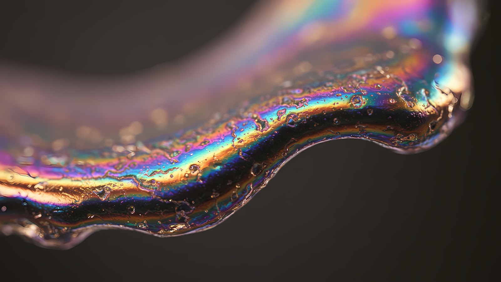 Download 4K macro iridescent liquid surface wallpaper, featuring a close-up shot of a clear liquid surface displaying a spectrum of rainbow colors and tiny droplets.
