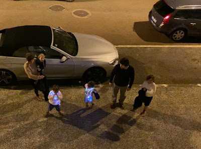 familia pipoca na rua no dia de Natal, com as camisolas de luzes na noite serrada a olhar para os primos lá em cima em casa fechados