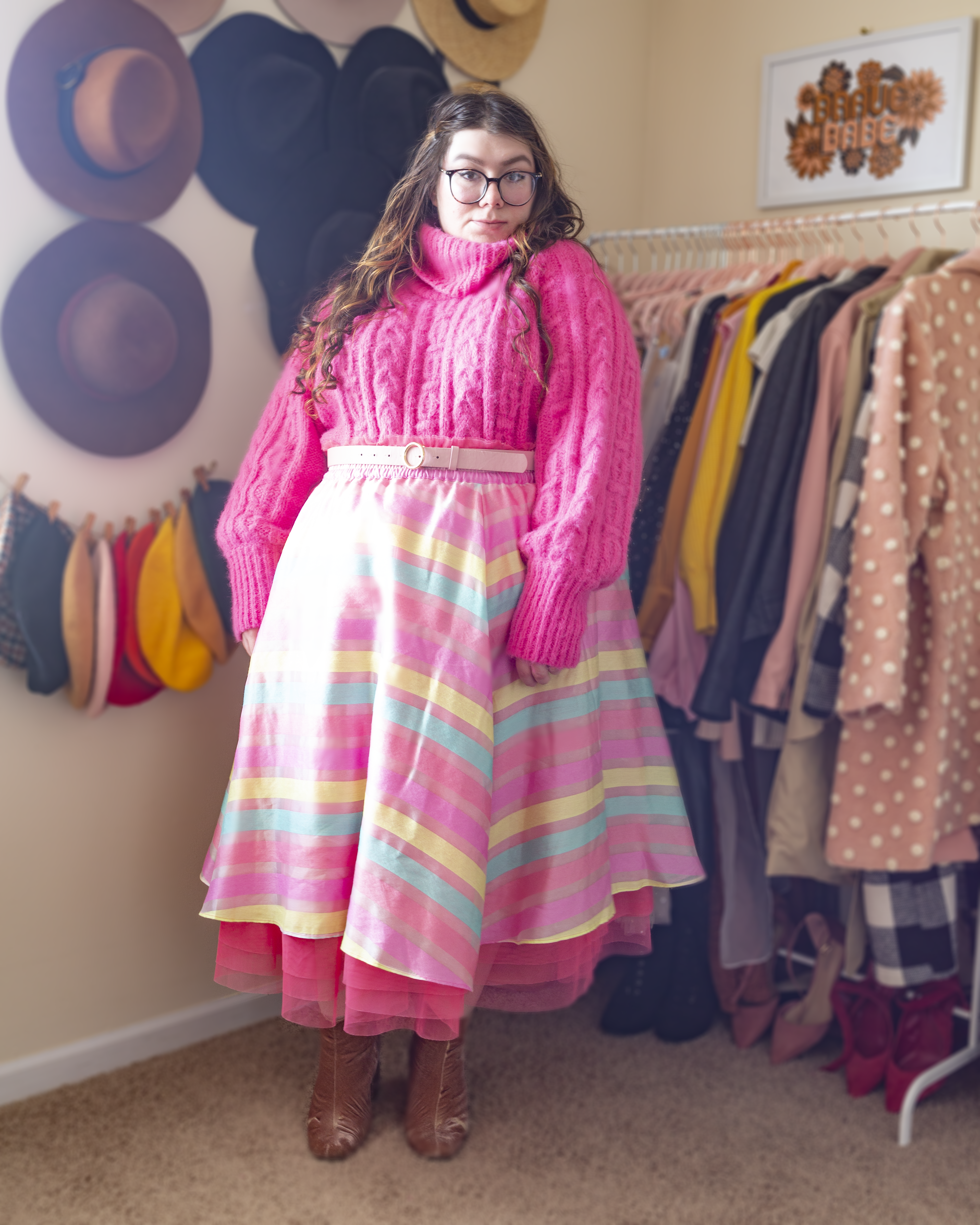 An outfit consisting of a bright pink turtleneck sweater tucked into a pastel pink, light blue and light yellow striped tulle midi skirt and pink heeled clogs.