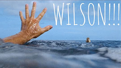 Tom Hanks hand pushing through the ocean towards a volleyball with a face floating away with the caption WILSON in large white letters