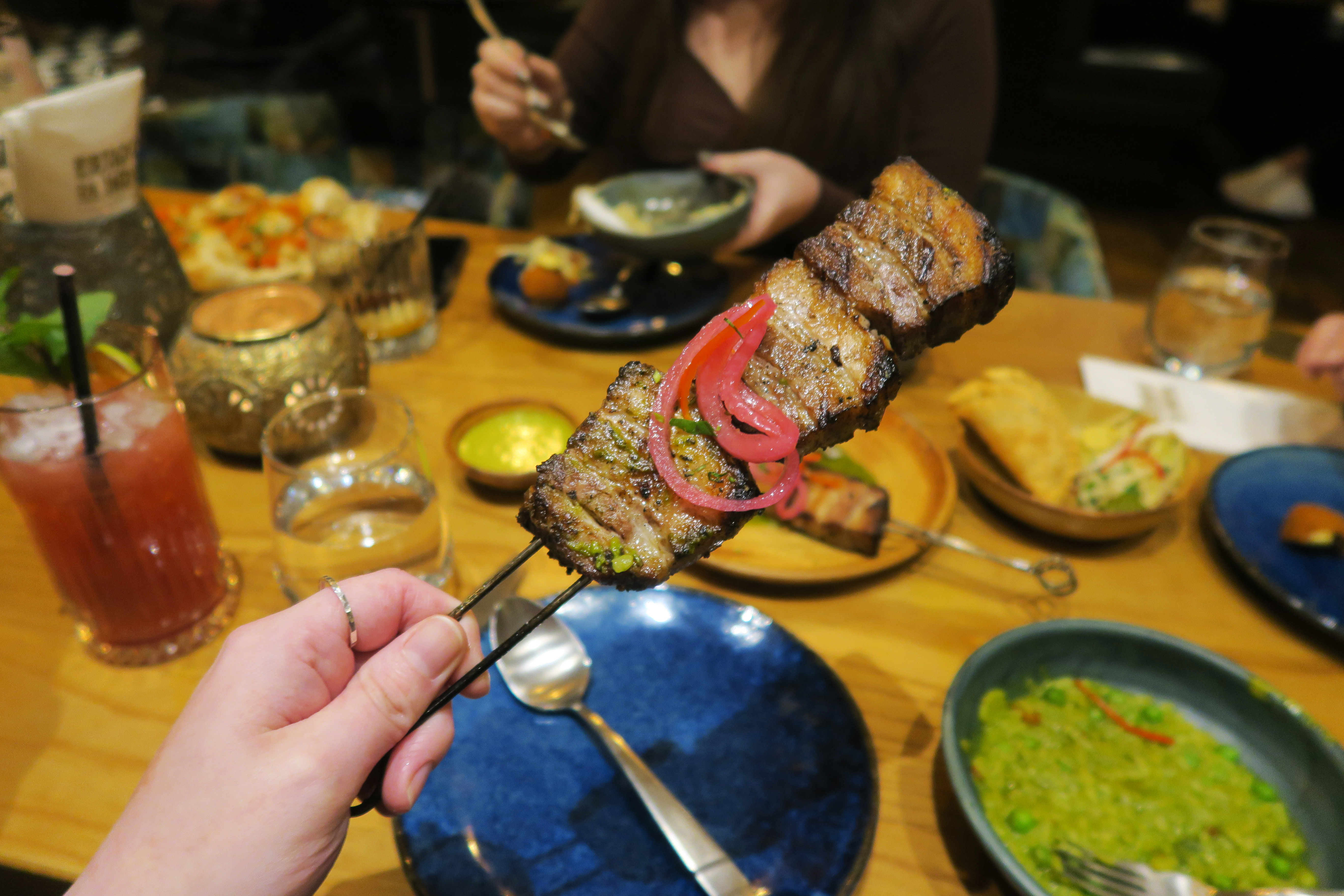 Holden a Pork belly skewer. Other dishes can be seen in the background