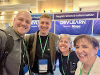 Photo of four smiling individuals in front of a conference registration desk with the Kineo logo behind them.