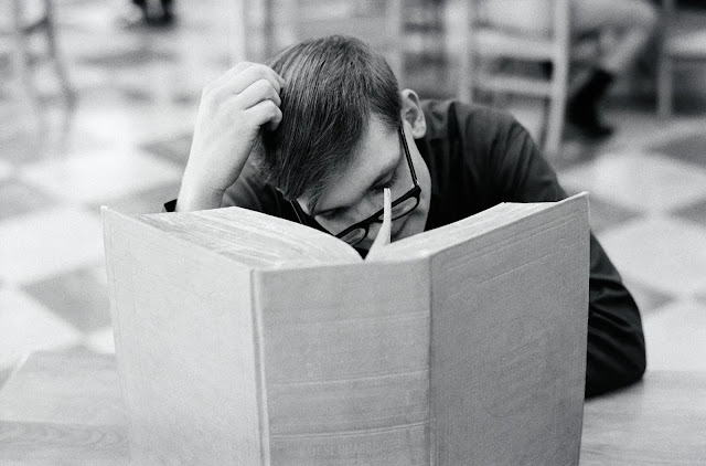 A man in glasses reading a giant book.