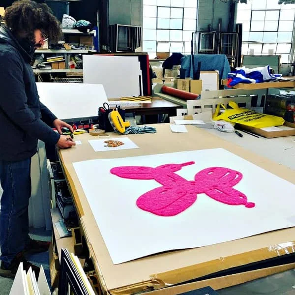 standing man working on quilled pieces displayed on table in frame shop