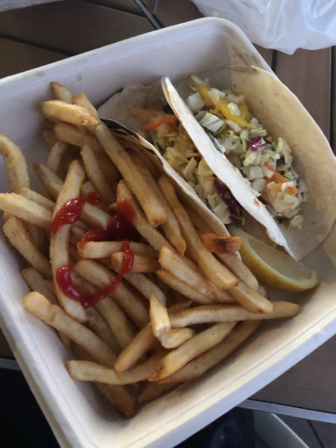 A clamshell container holding 2 fish tacos and french fries.