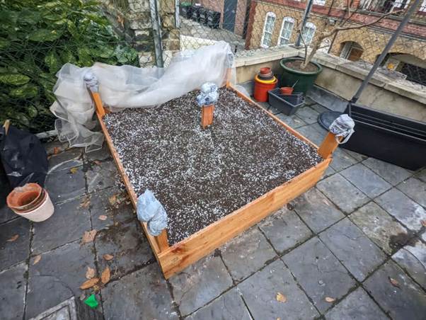 A wooden box with dirt and white plastic bags on a stone surface

AI-generated content may be incorrect.