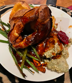 A roast dinner, including green beans, stuffing, roast potatoes and carrot. There's a big Yorkshire pudding on top and the whole thing's covered in gravy.