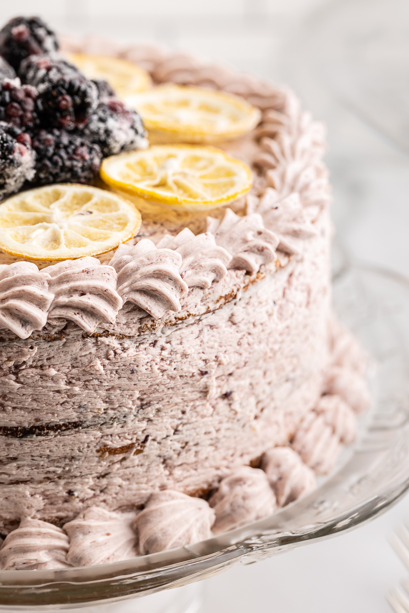 Closeup of Keto Lemon Cake with Blackberry Mascarpone Frosting on a glass cake stand.