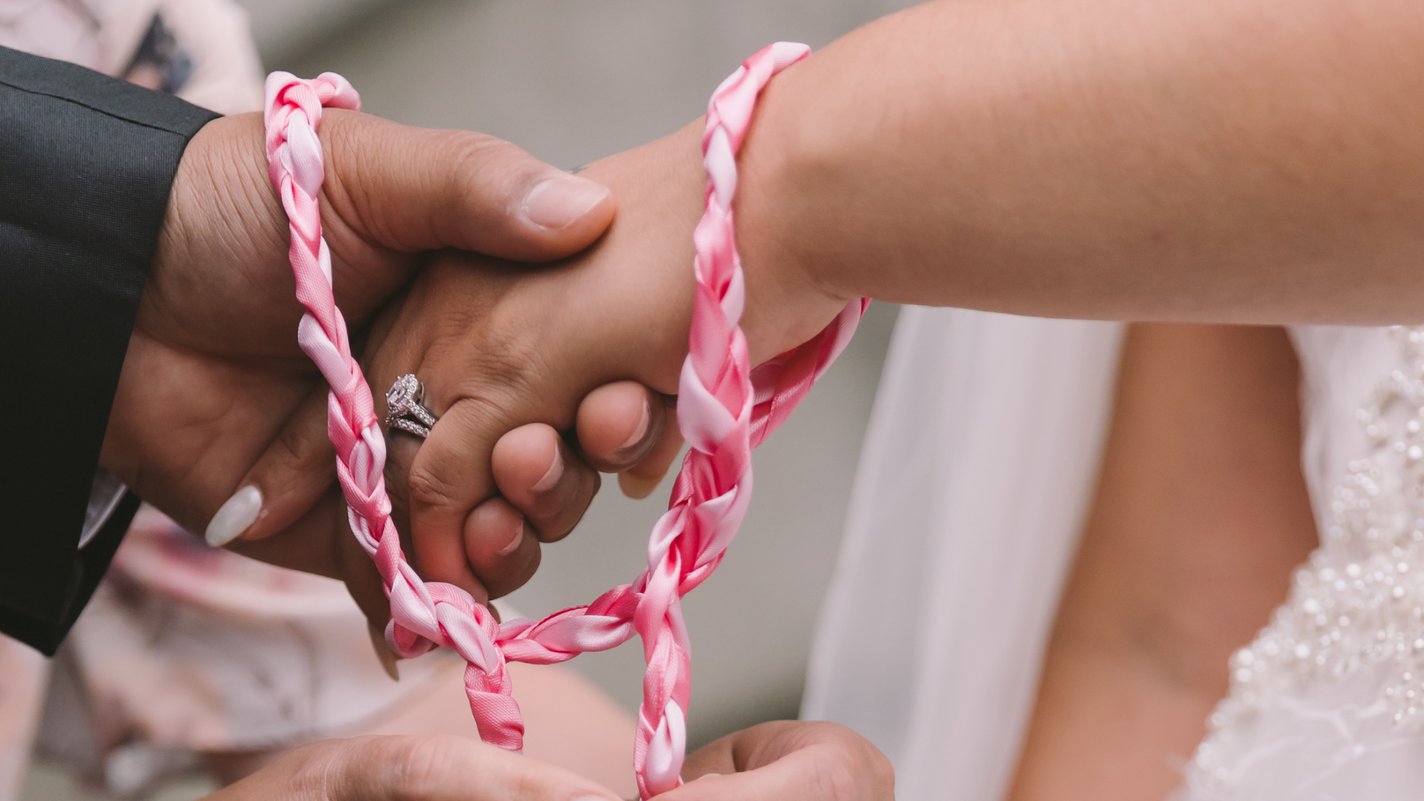 A close up of a handfasting ceremony with red and pink ribbons