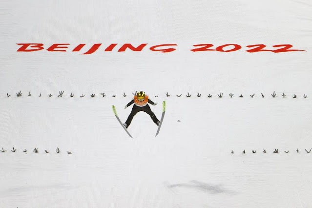 De colete laranja, Ursa Bogataj, salta com os dizeres Beijing 2022 em vermelho atrás dela