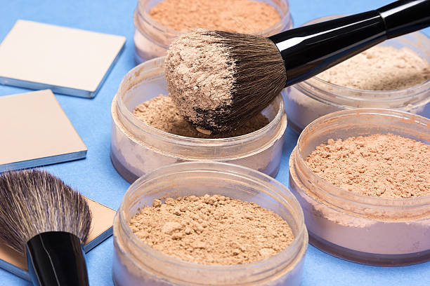 Makeup powders and brushes in jars on blue background.