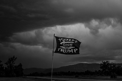 a black and white photo of a  flag near Red Lodge, Montana that says "God, Guns, Trump" Credit  Ashley Gilbertson